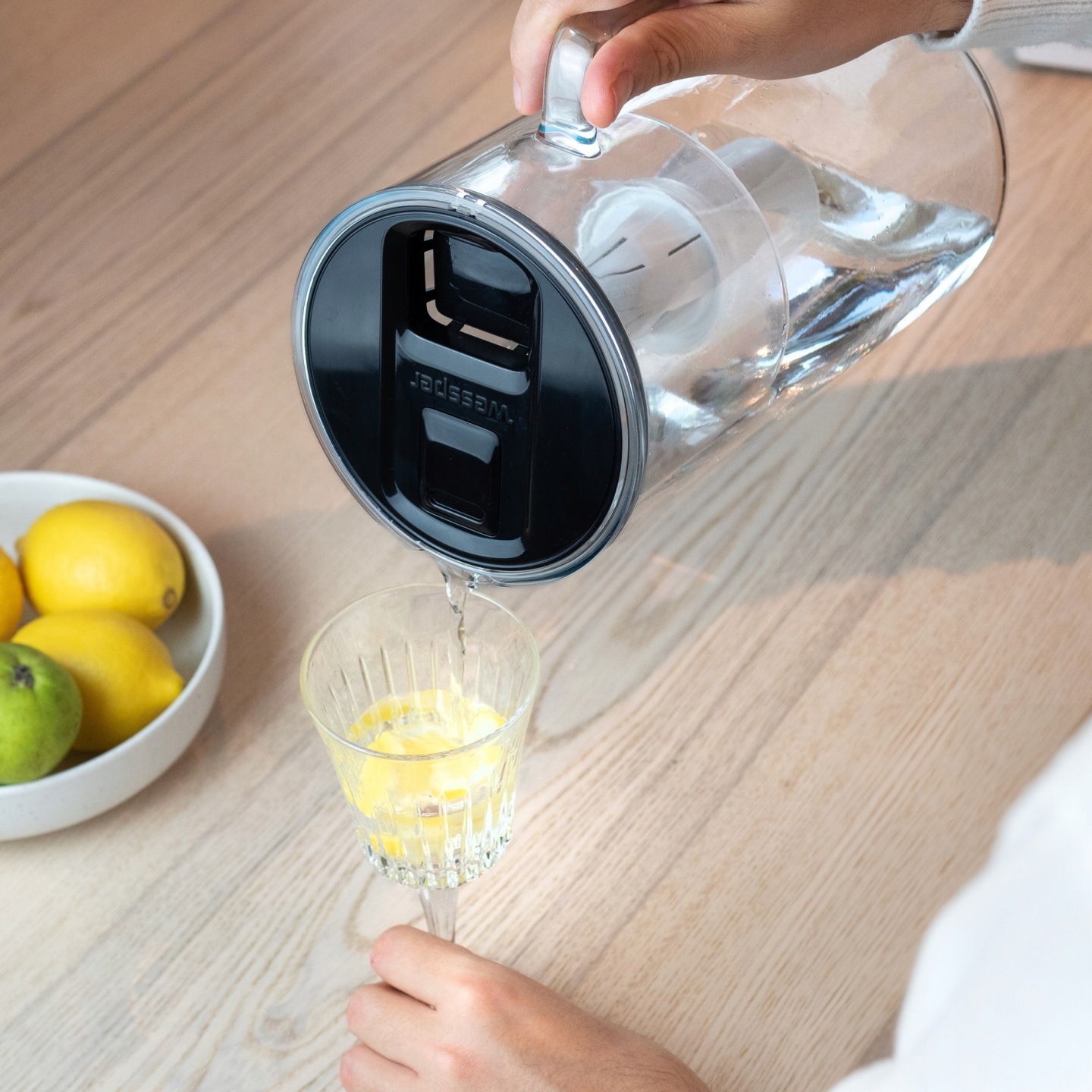 Kobieta nalewa przefiltrowaną wodę z dzbanka Wessper do wysokiego kieliszka z cytryną